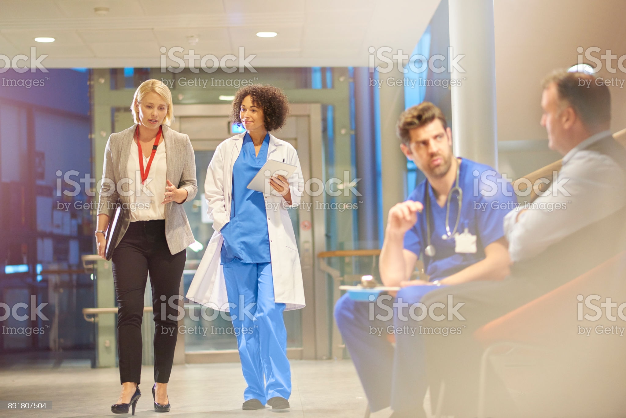 doctor-listening-to-sales-rep-in-hospital-corridor-picture-id891807504